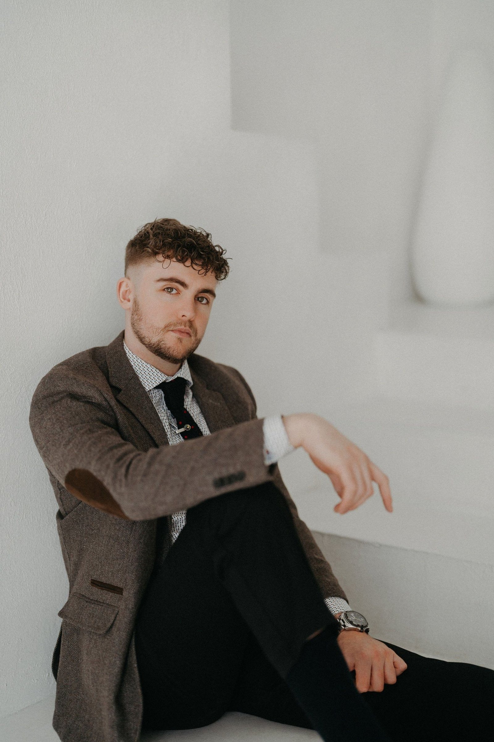 Portrait: tweed jacket, seated against a white wall